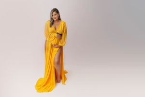 Elegant maternity portrait in flowing yellow dress against white background.
