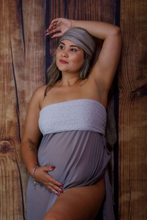 Maternity photo of person in gray dress and headwrap against rustic wooden backdrop.
