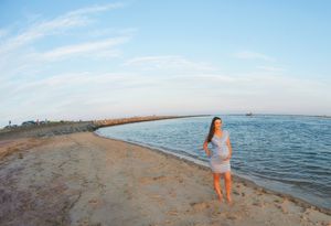 A silhouetted figure stands on a curving beach shoreline at dusk.