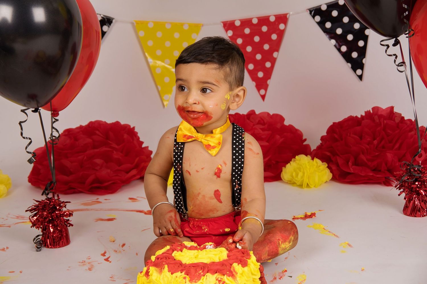 baby eating cake with mickey mouse decorations and balloons