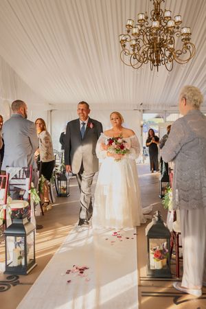 Wedding ceremony processional in elegant white tent venue with chandelier and aisle decorations.