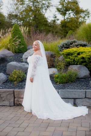 Elegant bridal portraits showing flowing train of white lace wedding dress in garden setting.