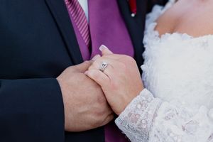 Close-up details of couple's embrace showing lace wedding dress and formal attire.