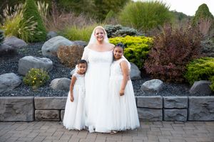 Bride in white lace gown poses on stone patio surrounded by lush garden landscaping.