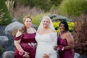Wedding party in burgundy dresses poses for photos in a garden setting.