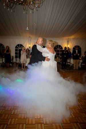 First dance at wedding reception with dramatic fog effect and colored lighting on dance floor.
