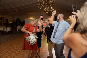 Wedding reception party with guests dancing under chandeliers in a decorated white venue.