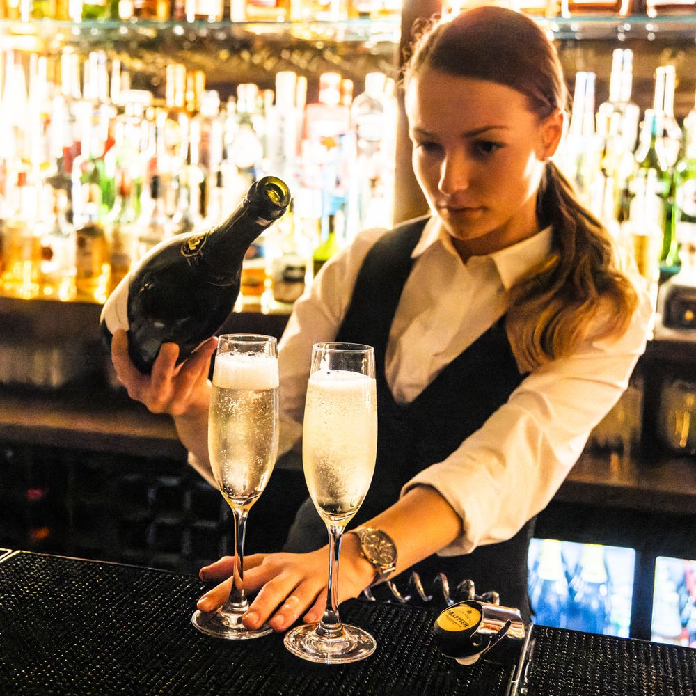 Mixologist pouring champagne in high-end cocktail bar | Branding image.