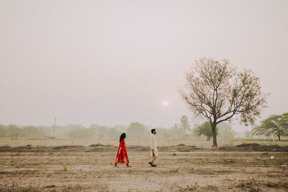 Two people in silhouette walk across a misty barren field with a lone tree on the horizon at dawn.