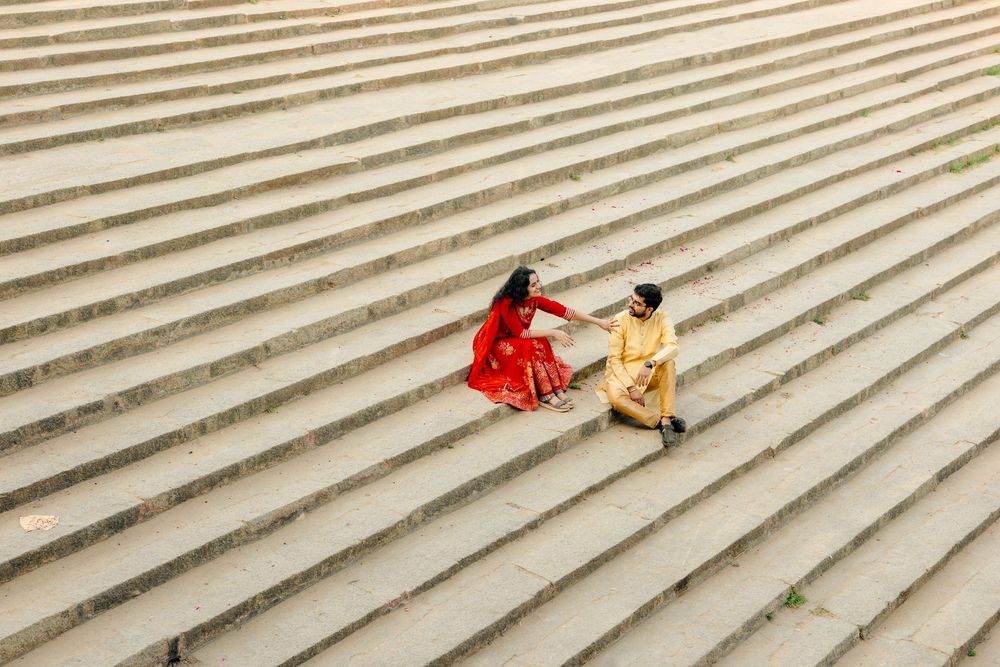 Two people in bright dresses sit together on wide concrete steps, viewed from above in a minimalist composition.