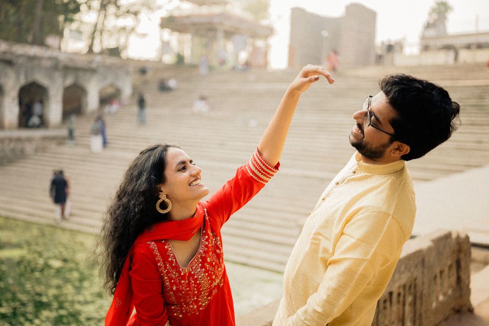 Two people share a playful moment on outdoor stone steps with one pointing up while wearing red and yellow outfits.