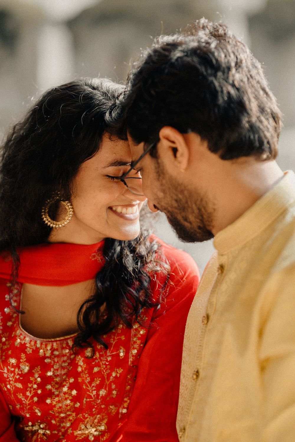 A close-up romantic moment between a couple in traditional Indian attire, with her in red and him in yellow.