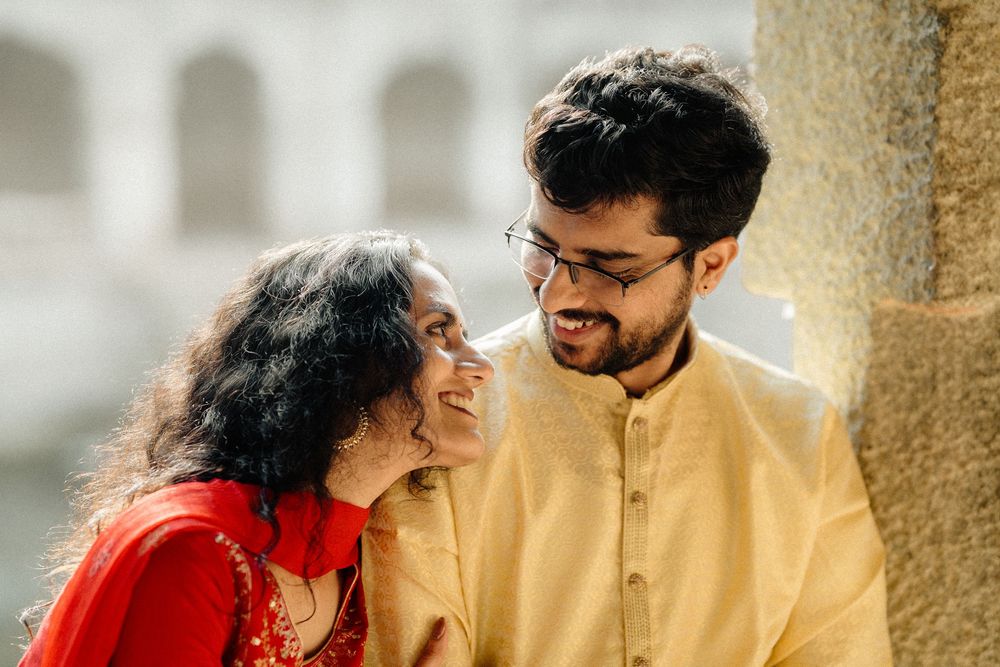 A couple in traditional South Asian attire share tender moments against a stone pillar backdrop.