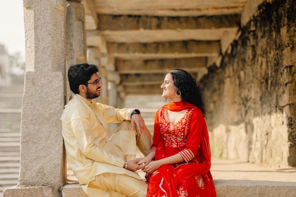 A couple in traditional attire shares a romantic moment against a stone architectural backdrop.
