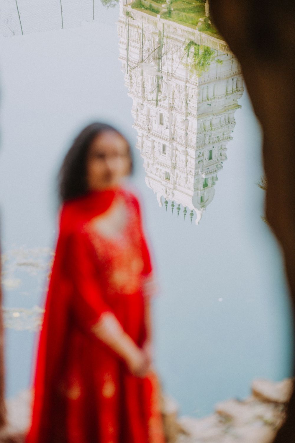 A person wearing a vibrant red traditional Indian sari stands against a light blue wall with hanging crystal decorations.