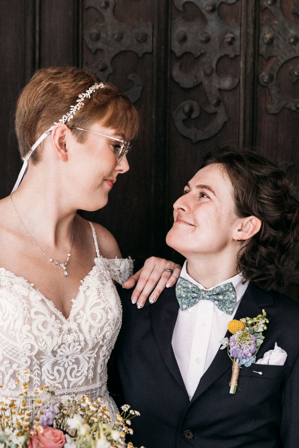 A tender moment between a couple in wedding attire against an ornate wooden backdrop.