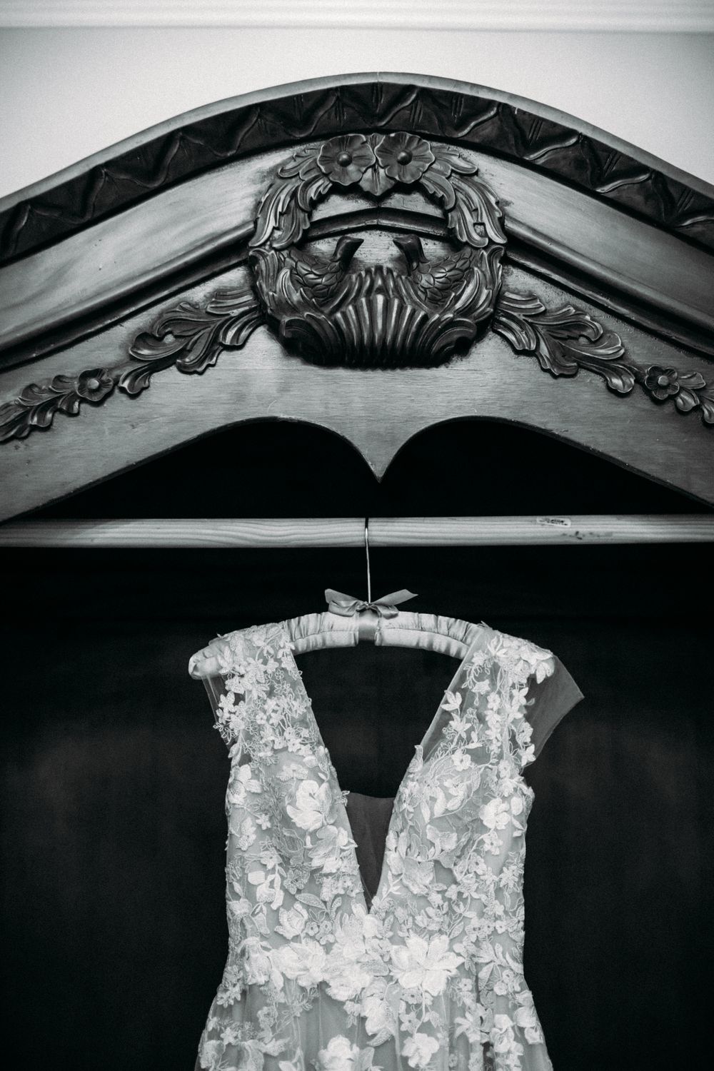 Black and white photo of ornate wedding dress hanging beneath decorative architectural detail.