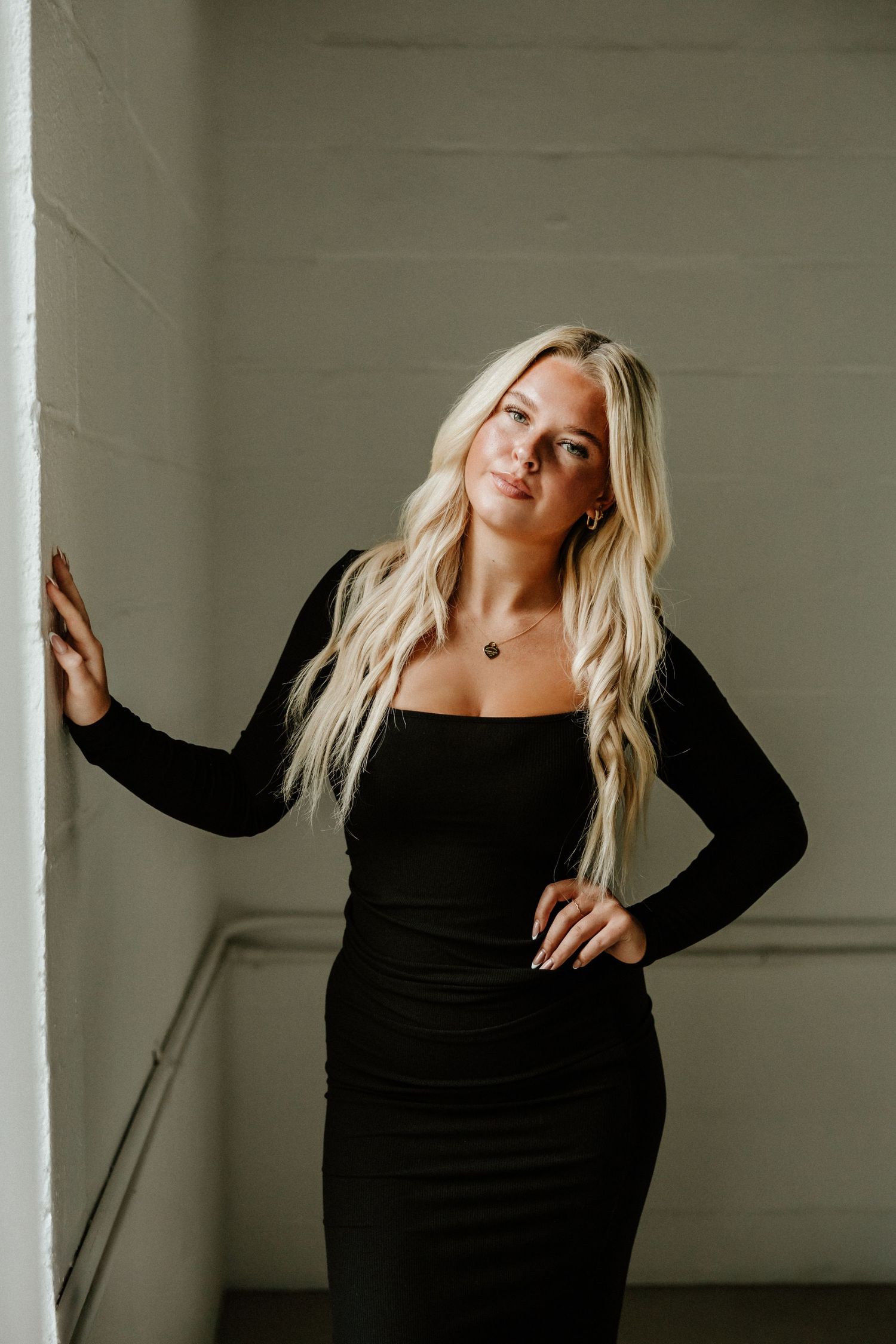 Stylish figure-hugging black dress against white wall in modern fashion photography.