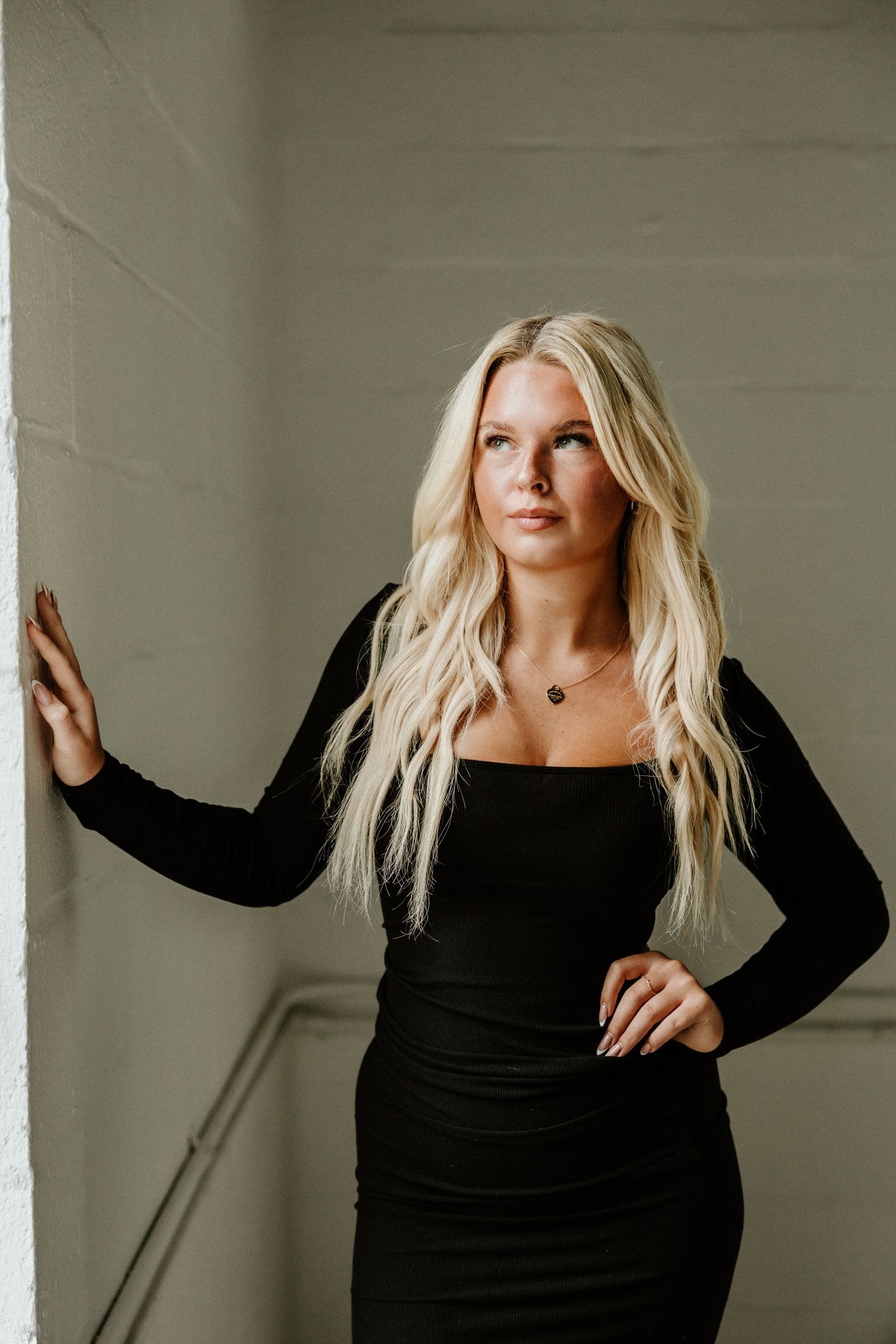 Long-sleeved black bodycon dress worn in minimalist indoor photoshoot.