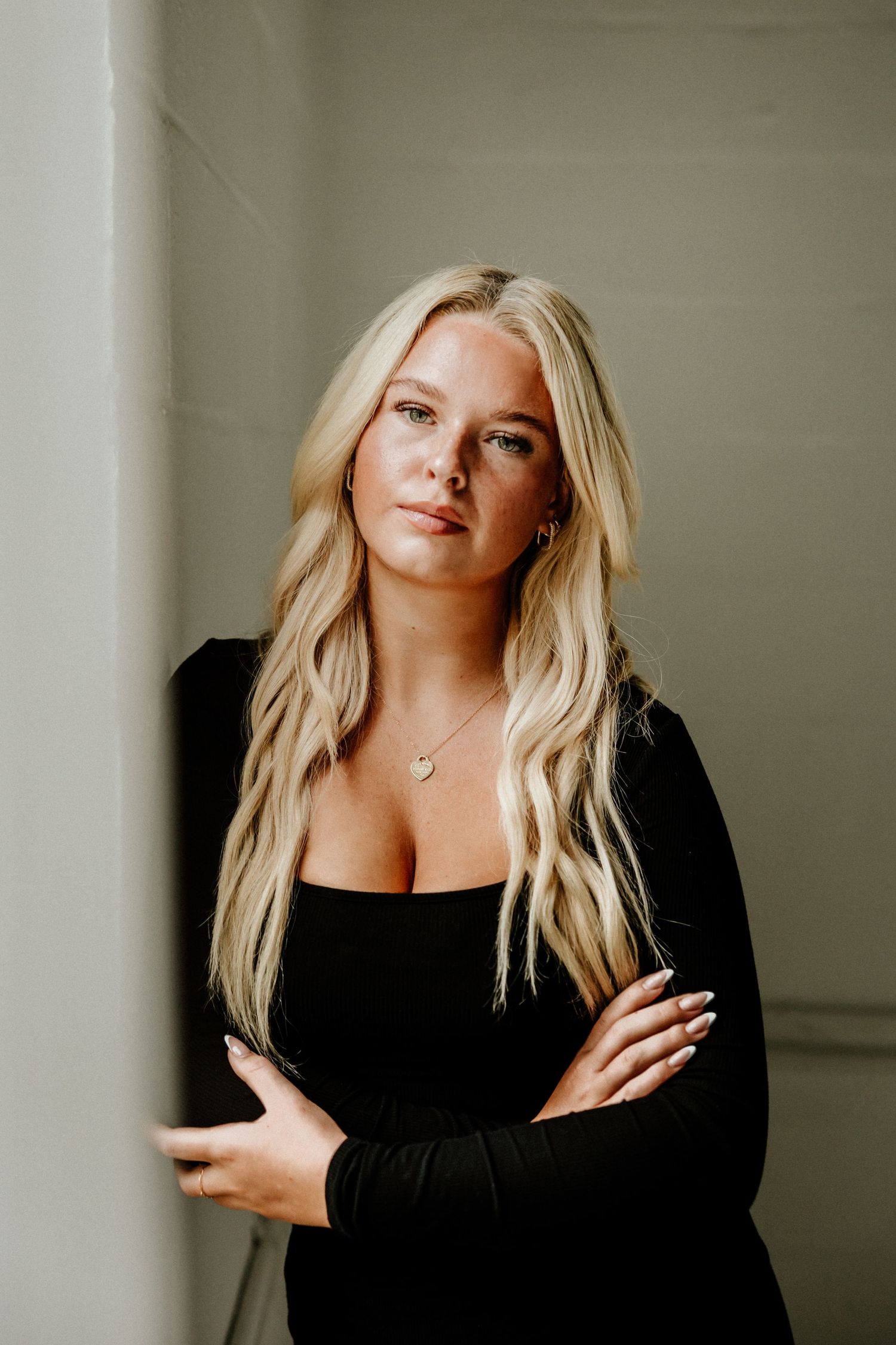Professional portrait in black long-sleeve dress against neutral wall background.