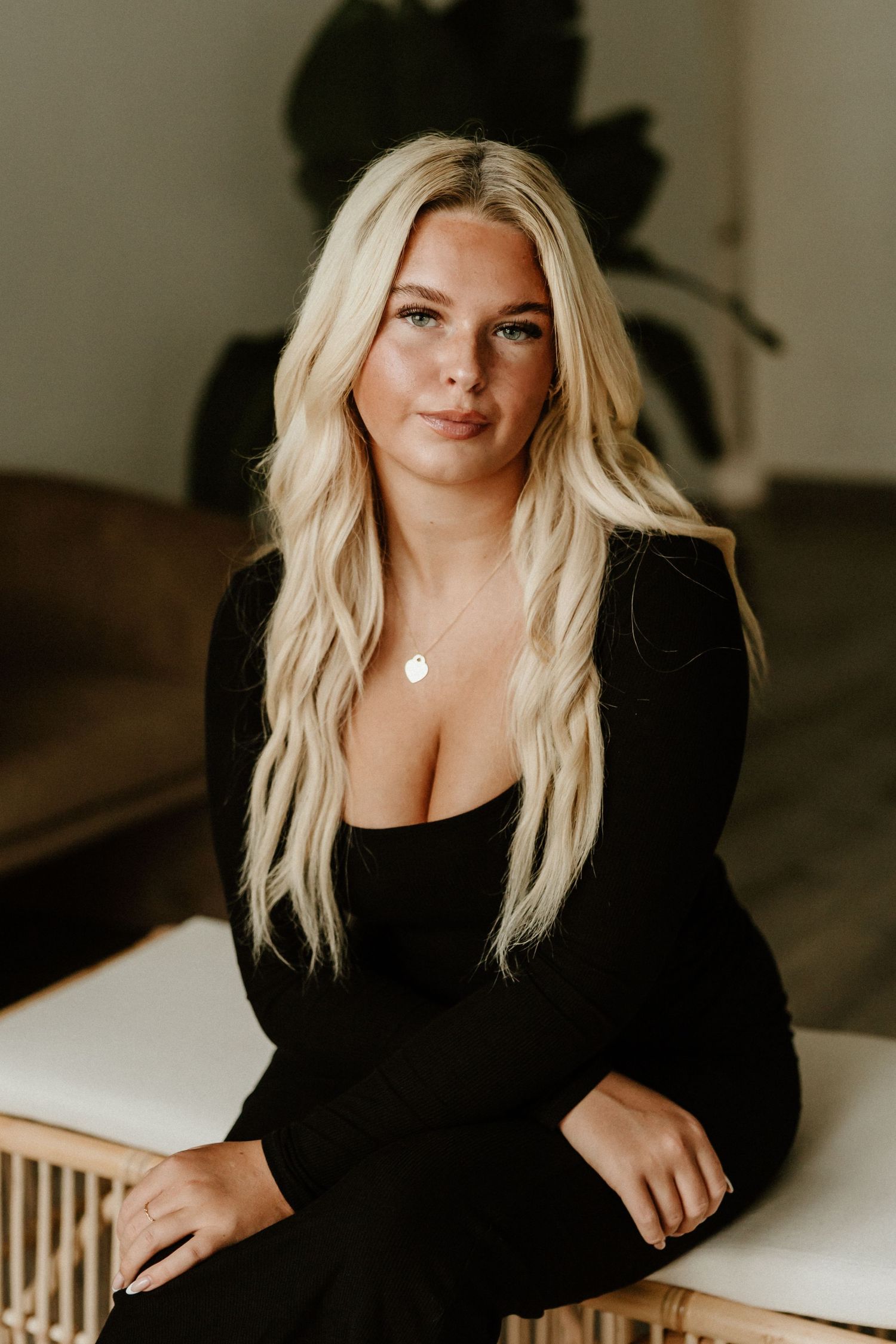 Warm-toned indoor portrait featuring black long-sleeve dress and delicate necklace.