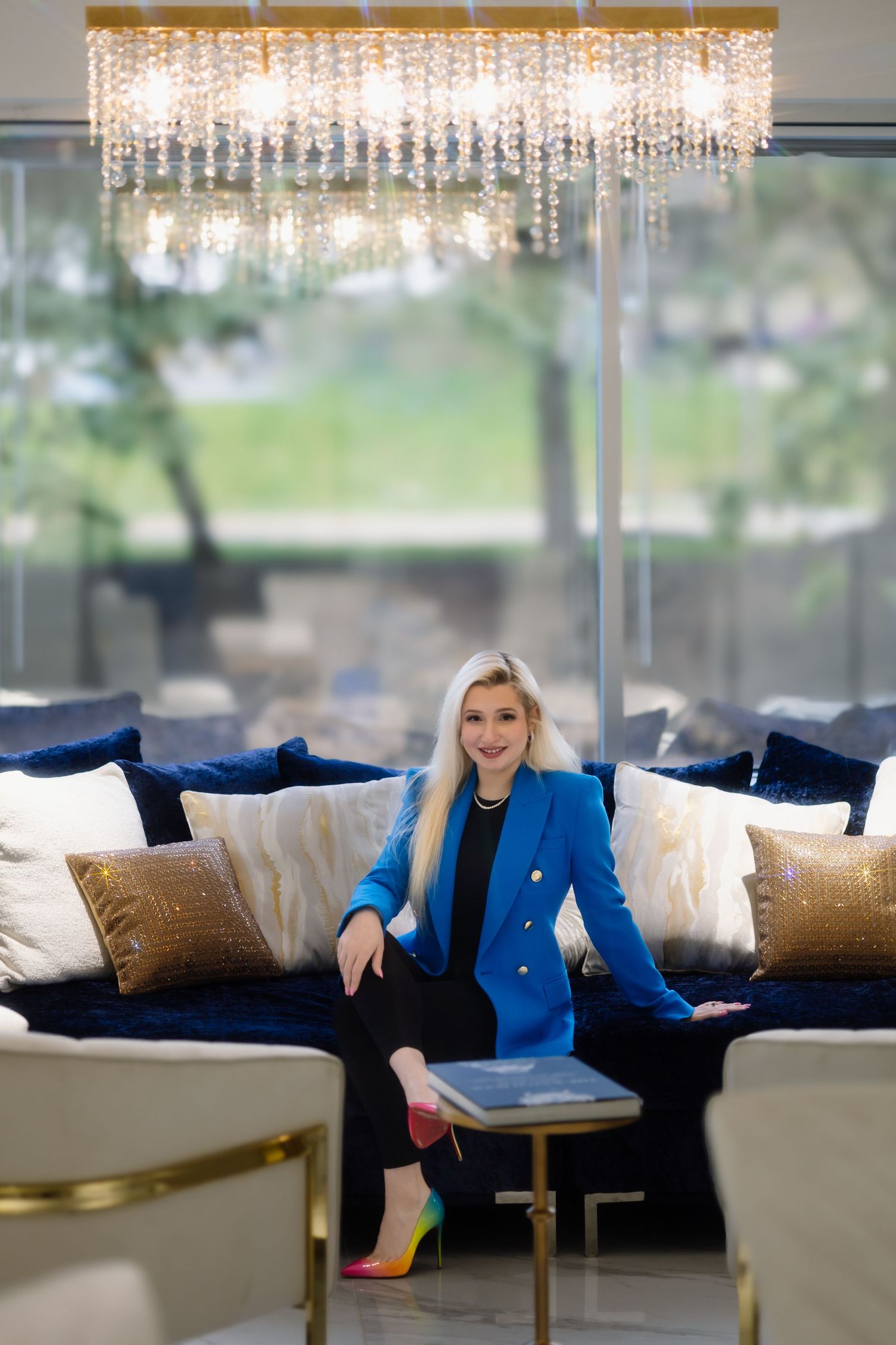 Modern luxury interior with crystal chandelier and person in blue blazer seated on navy velvet sofa.