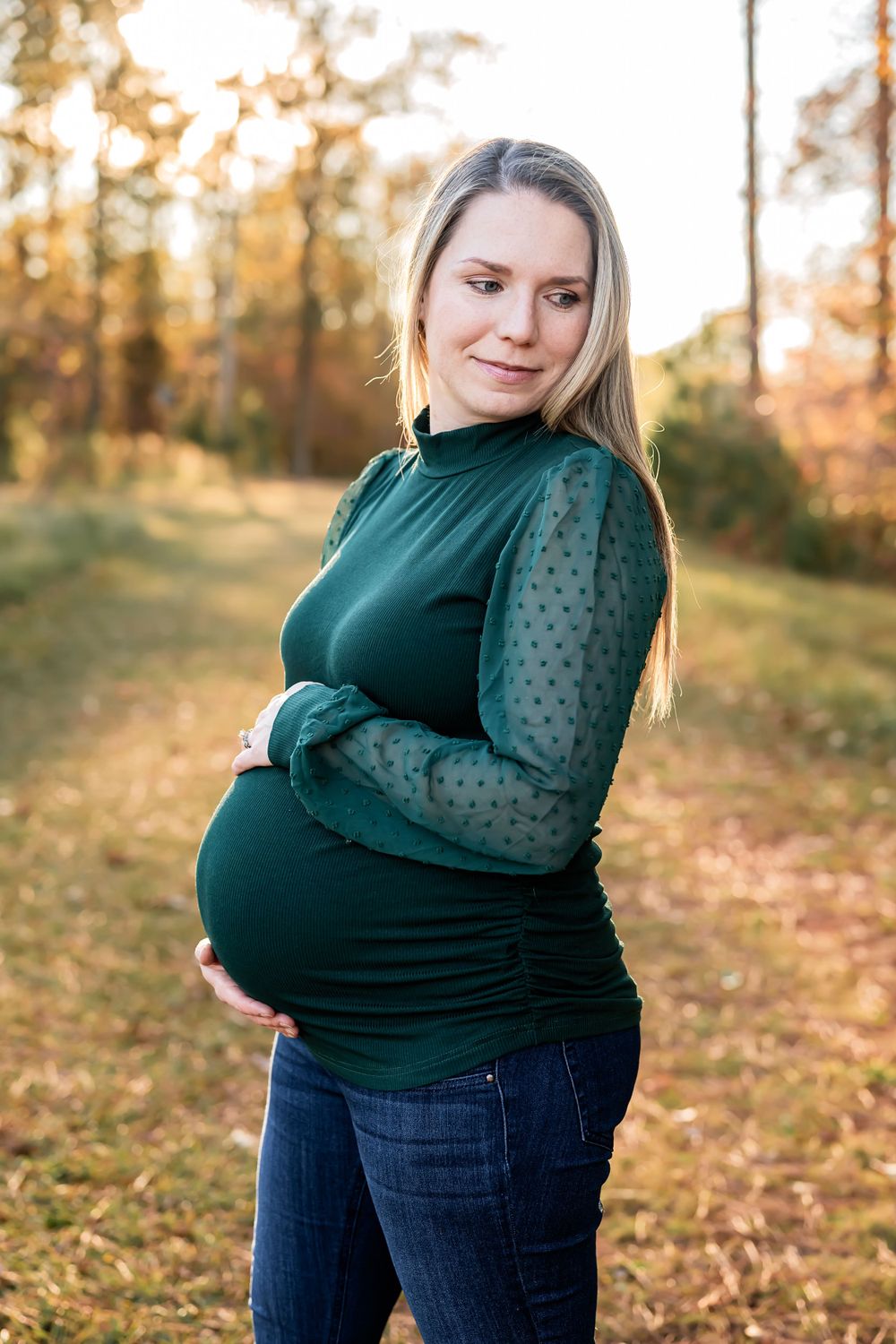 Expectant mother in green sweater poses in autumn forest setting.