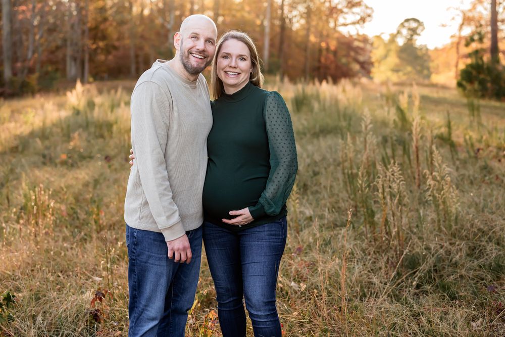 Couple poses together during maternity photoshoot in golden autumn forest.