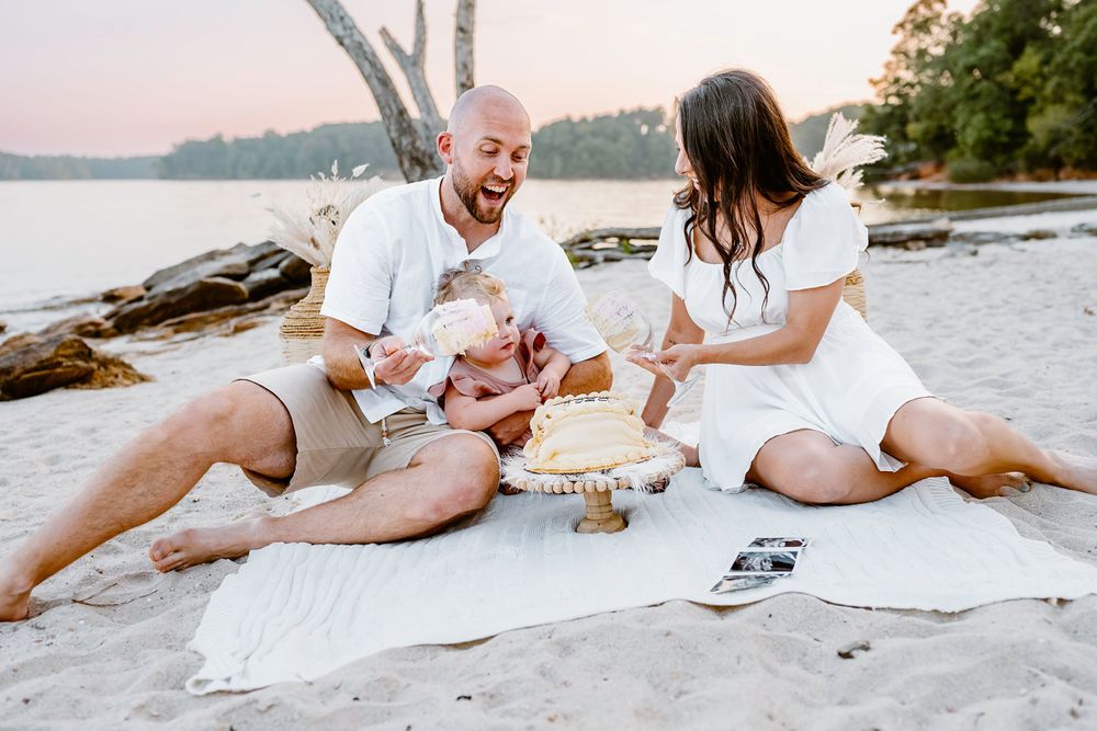 Family shares joyful moment during outdoor photoshoot on beach blanket.