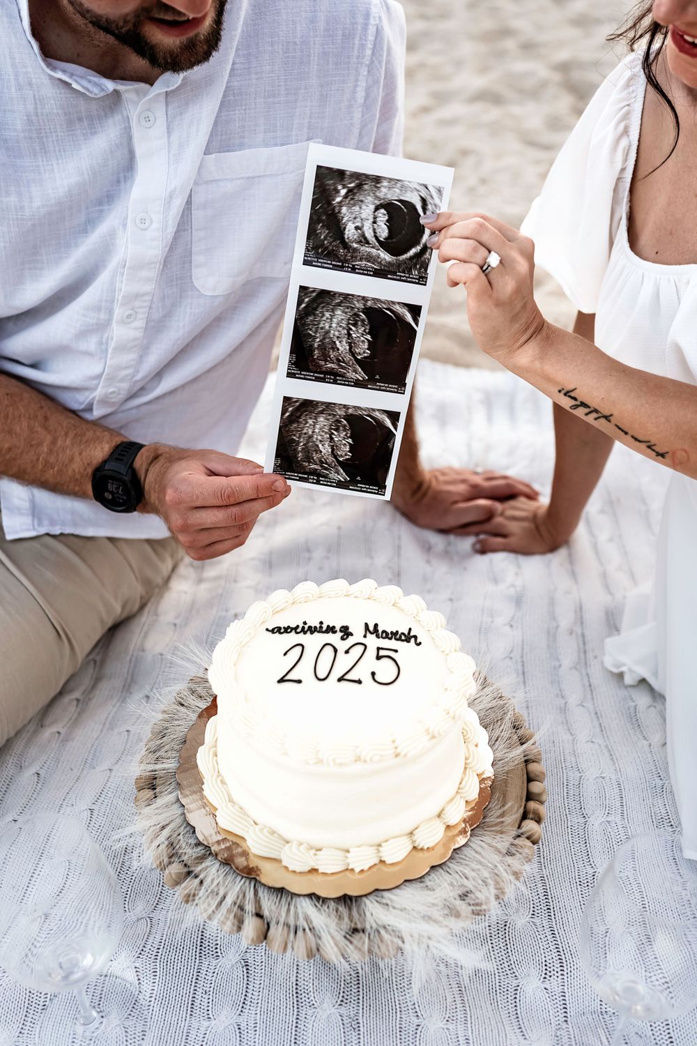 Couple holds ultrasound photos next to white cake with '2025' written on it.