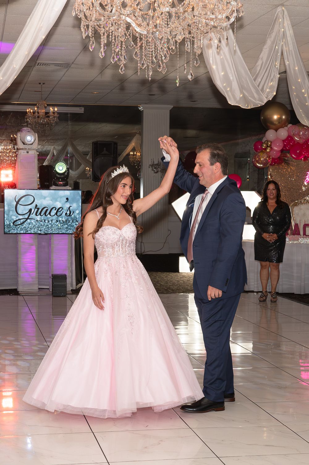 Couple dancing under crystal chandelier at an elegant reception venue with pink decor.