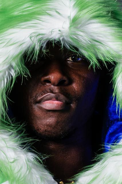Portrait wearing green and white furry hood against blue backdrop.