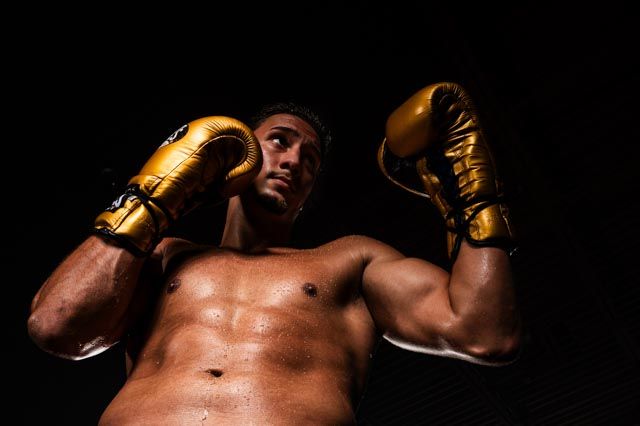 Dramatic low-key portrait of boxer with gold gloves against dark background.