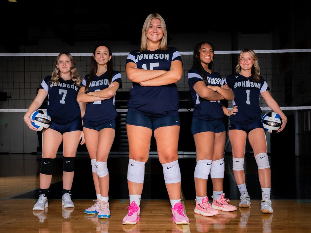 Row of volleyball players sitting on floor showing team shoes and socks.