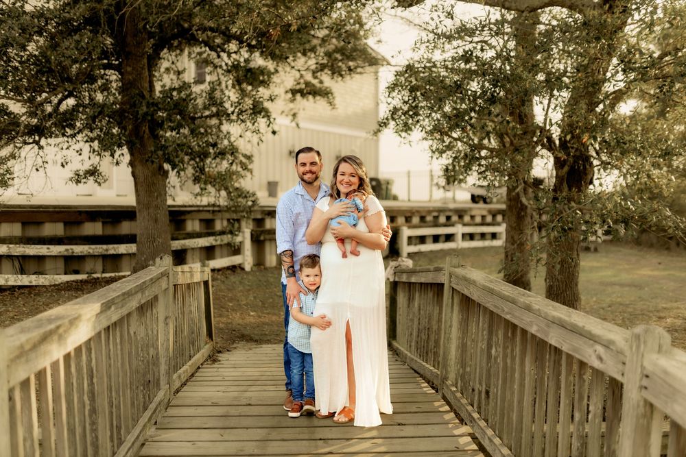 Family of four posing on wooden bridge surrounded by trees during maternity photo session outdoors.