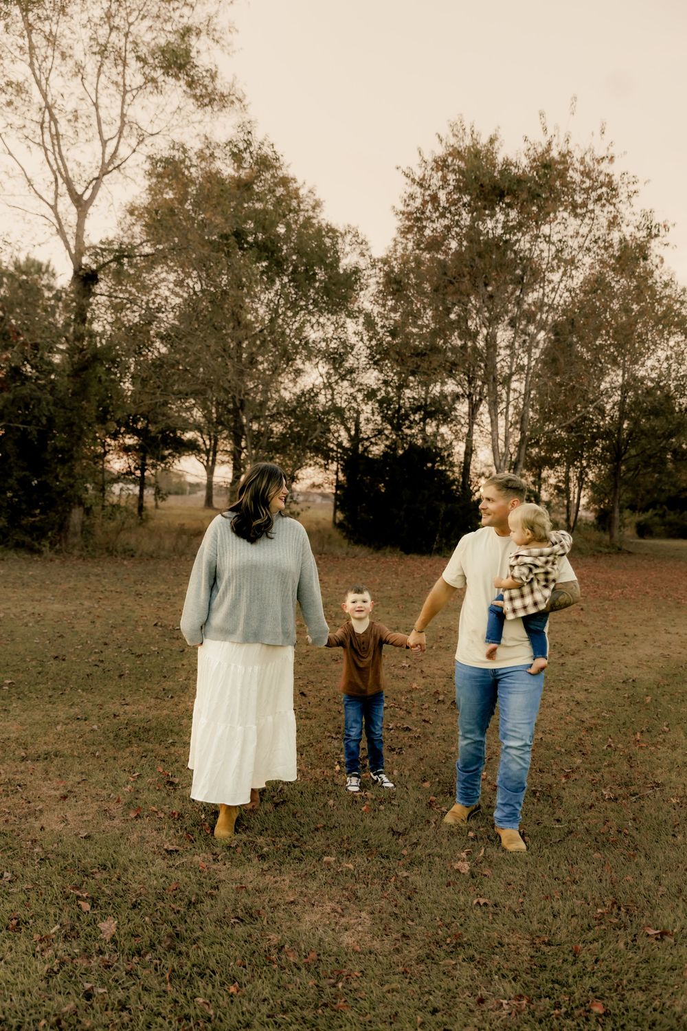 Family walking together through an autumn field at sunset in casual attire.