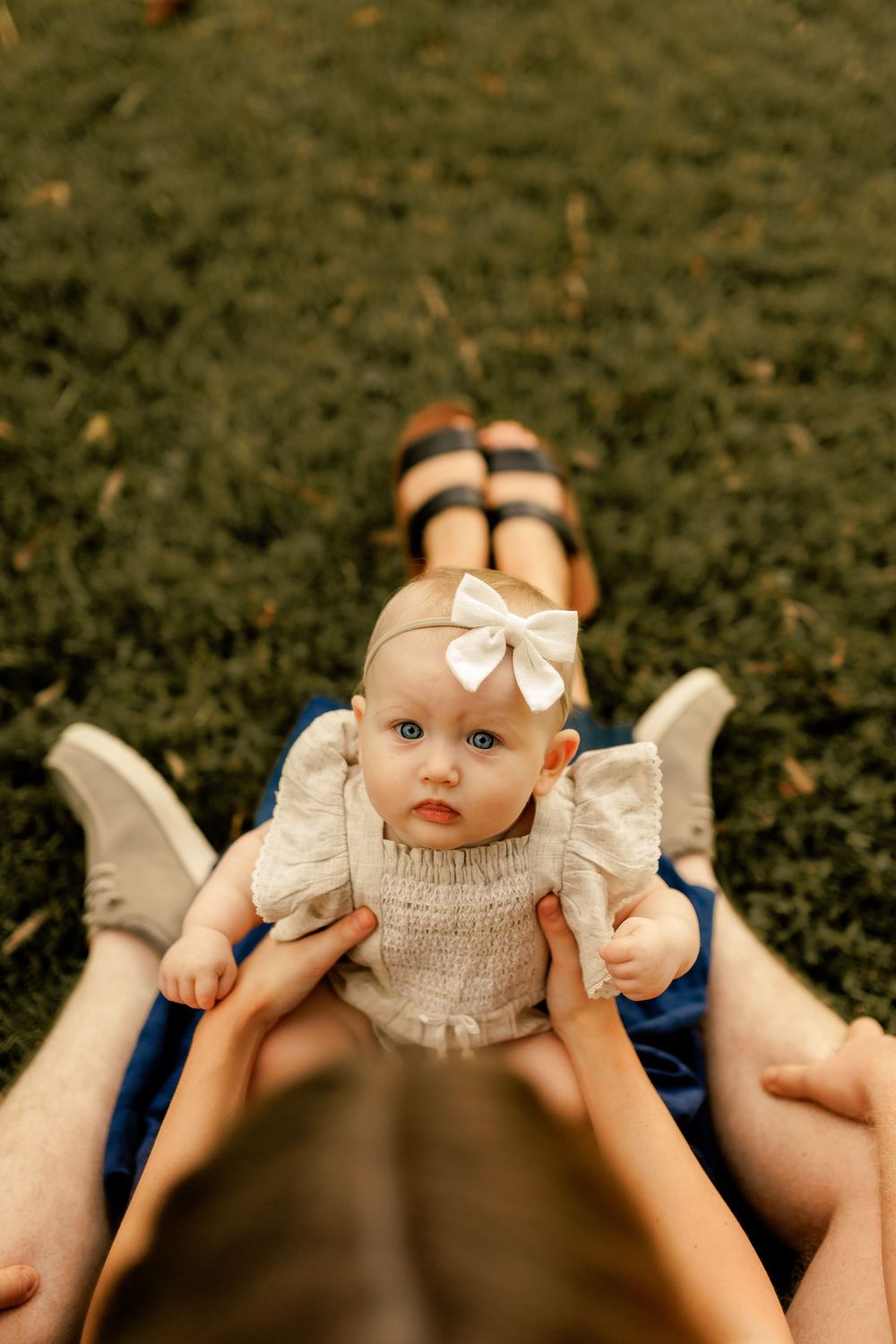 Overhead view of baby wearing white dress and bow during outdoor photo session.