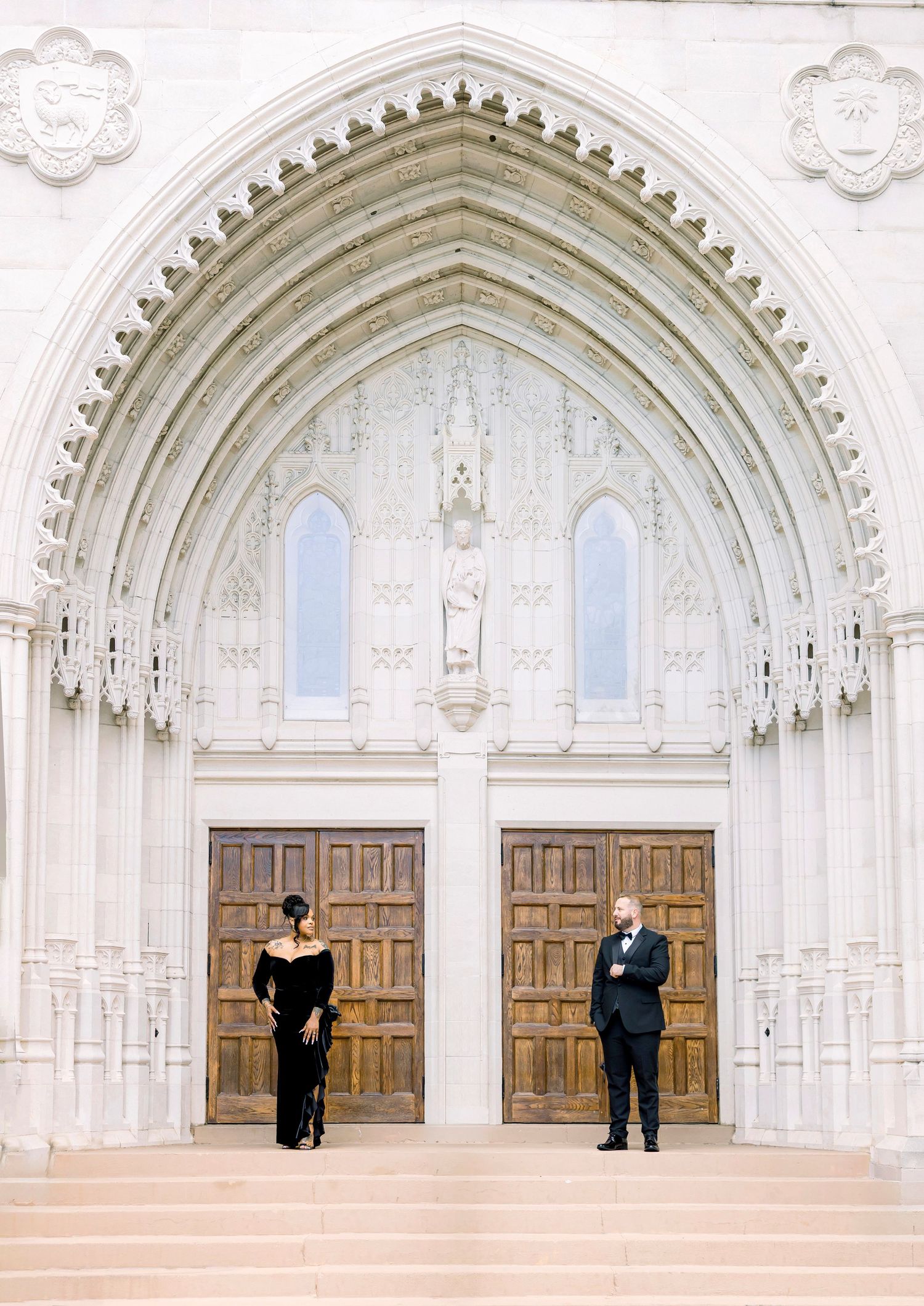 A dressed-up couple embraces against a bright blue building with outdoor lighting.
