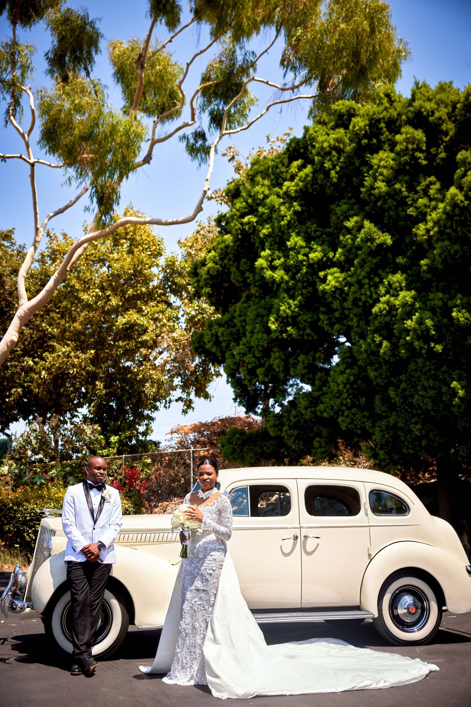 A classic white vintage car is decorated for a wedding with elegant drapery and floral arrangements in an outdoor setting.