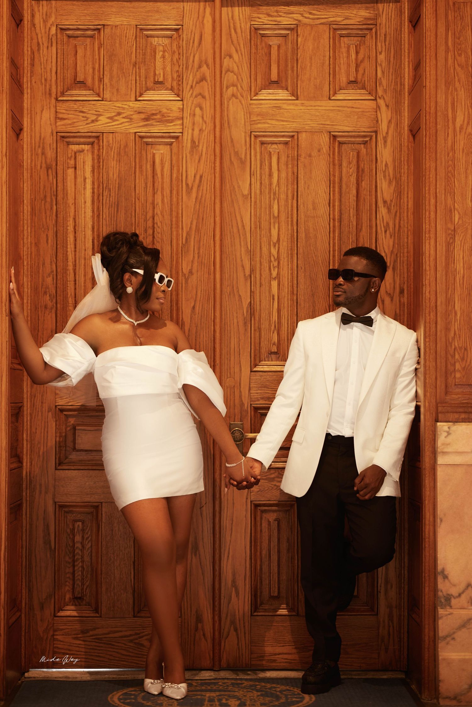 People in formal black and white attire pose playfully against a wooden paneled wall in an artistic composition.
