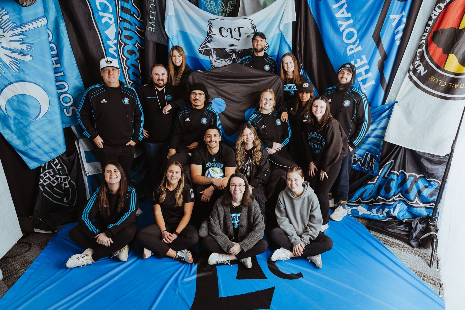 Group of Charlotte FC soccer fans posing with blue team banners and flags.