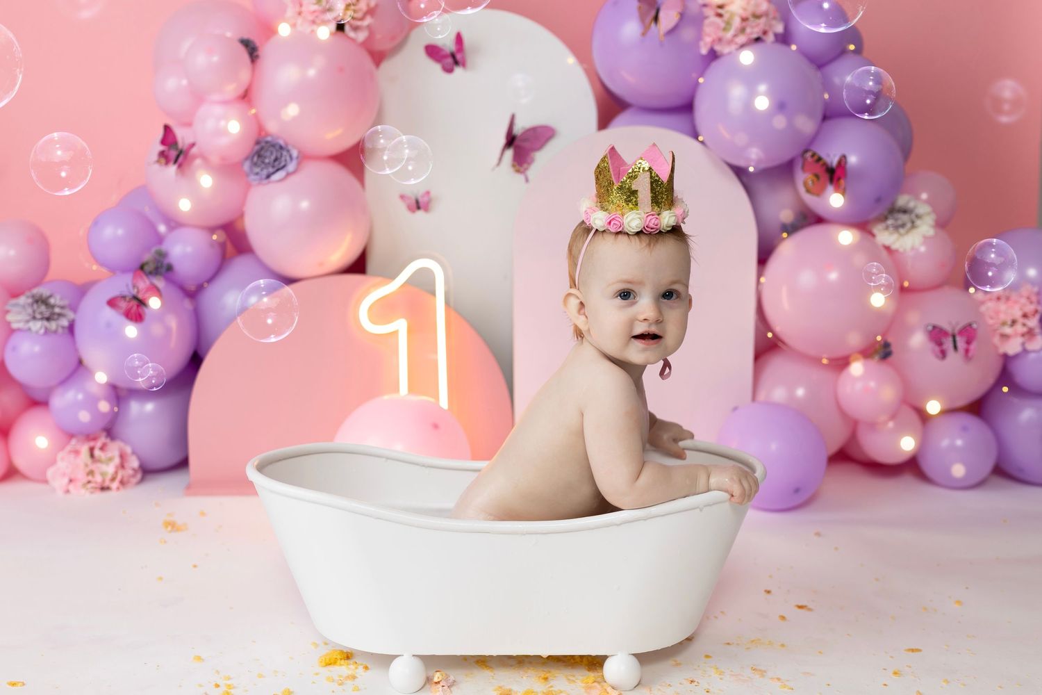 Baby bath photo setup with colorful balloon backdrop and white tub prop.