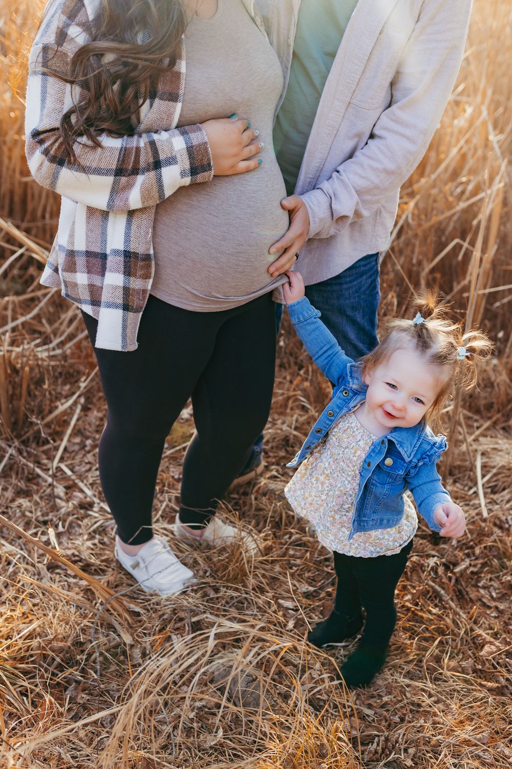 Excited big sister gently touching her mom’s baby bump while her parents stand together during their maternity session in Wisconsin.