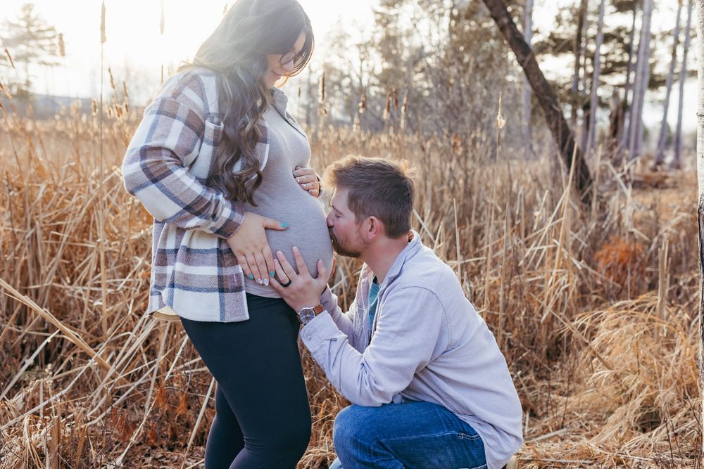Expectant father kissing mother’s baby bump during an outdoor maternity session in Wisconsin.