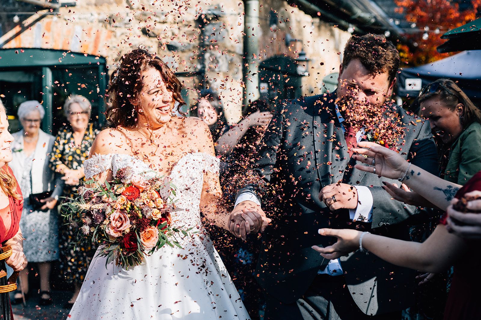 Wedding guests throw orange and red autumn leaves at a couple during an outdoor fall celebration.
