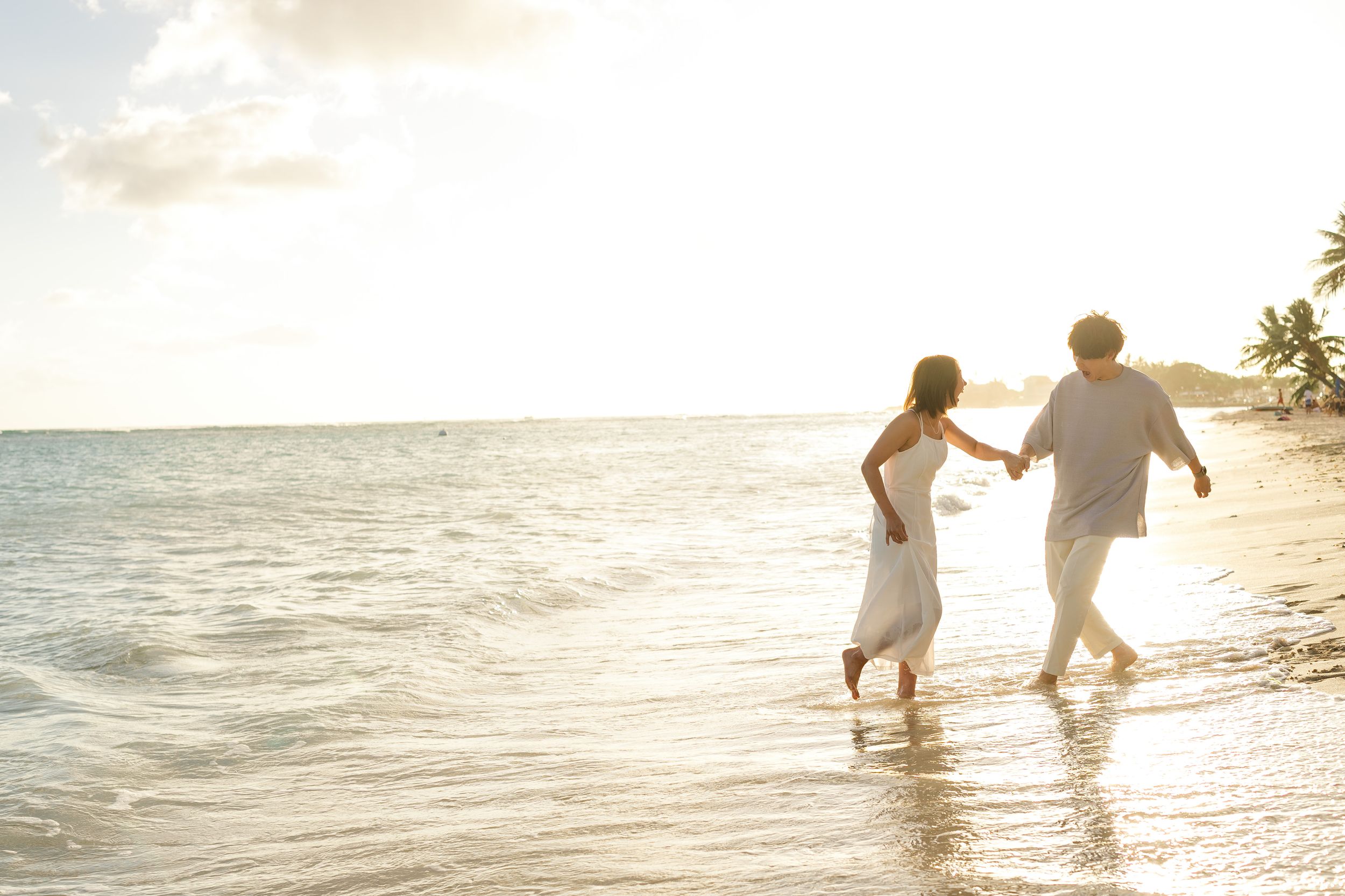 Couple walking hand in hand along the beach shoreline during golden hour.