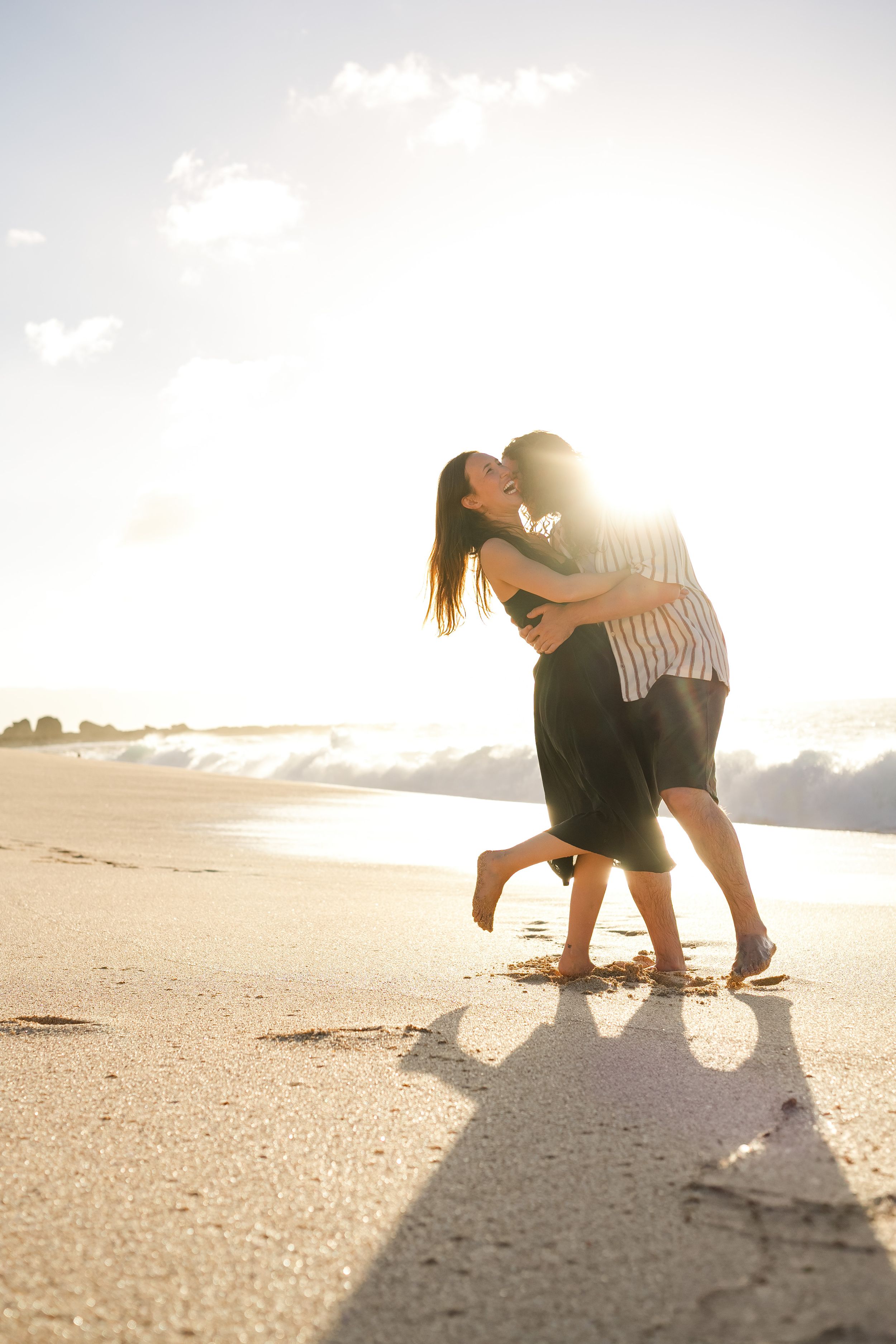 A couple dances on the beach during golden hour with their shadows visible on the sand.