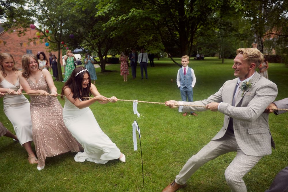 Wedding party dances playfully on green lawn during outdoor summer celebration.