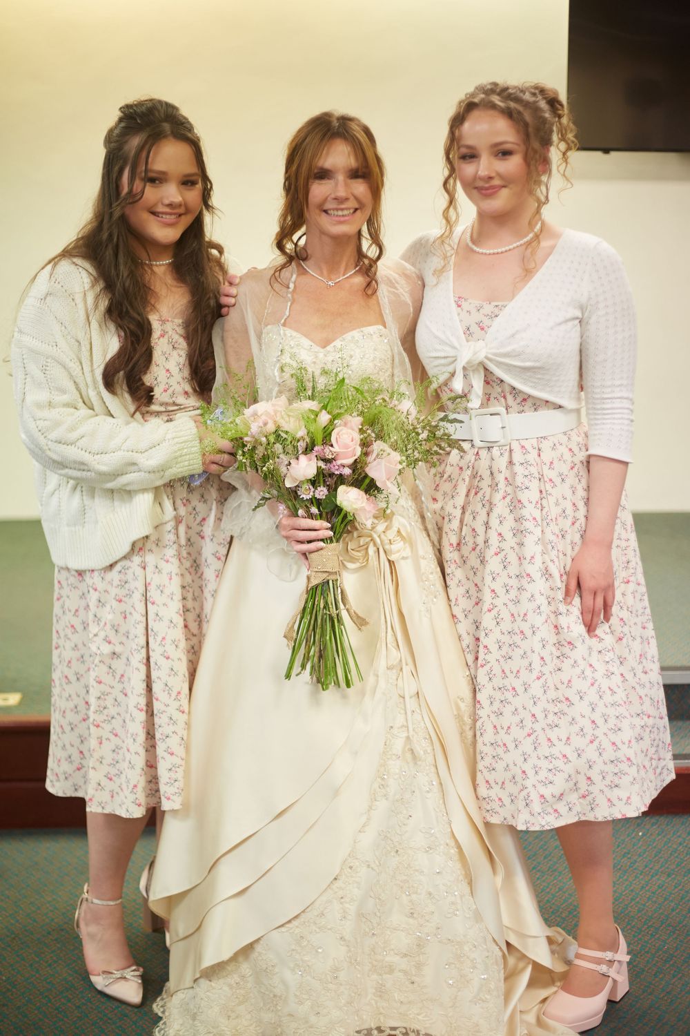 Three women pose together in vintage-style dresses and sleepwear at what appears to be a wedding celebration.