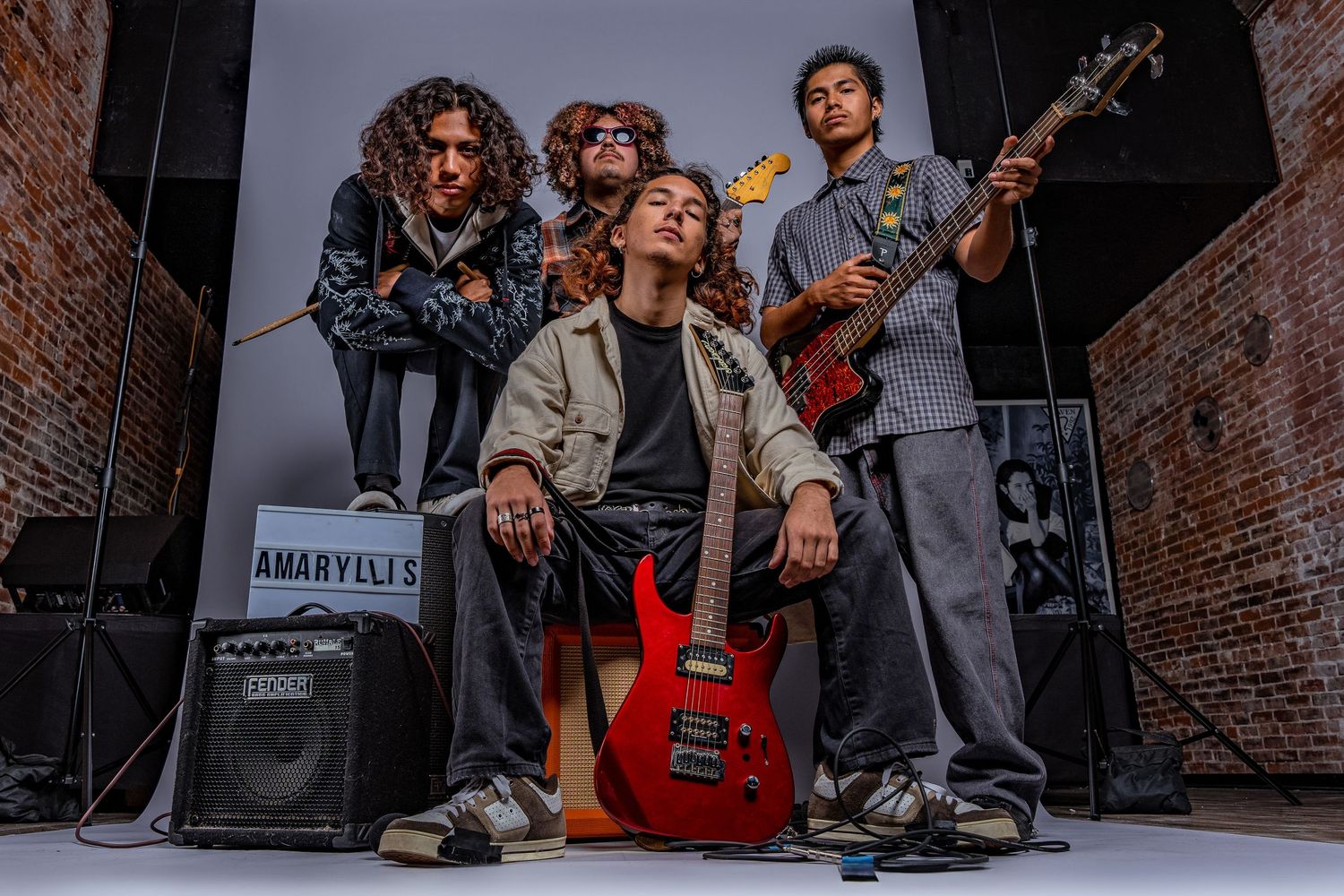 Rock band members posing with instruments in front of brick wall backdrop.